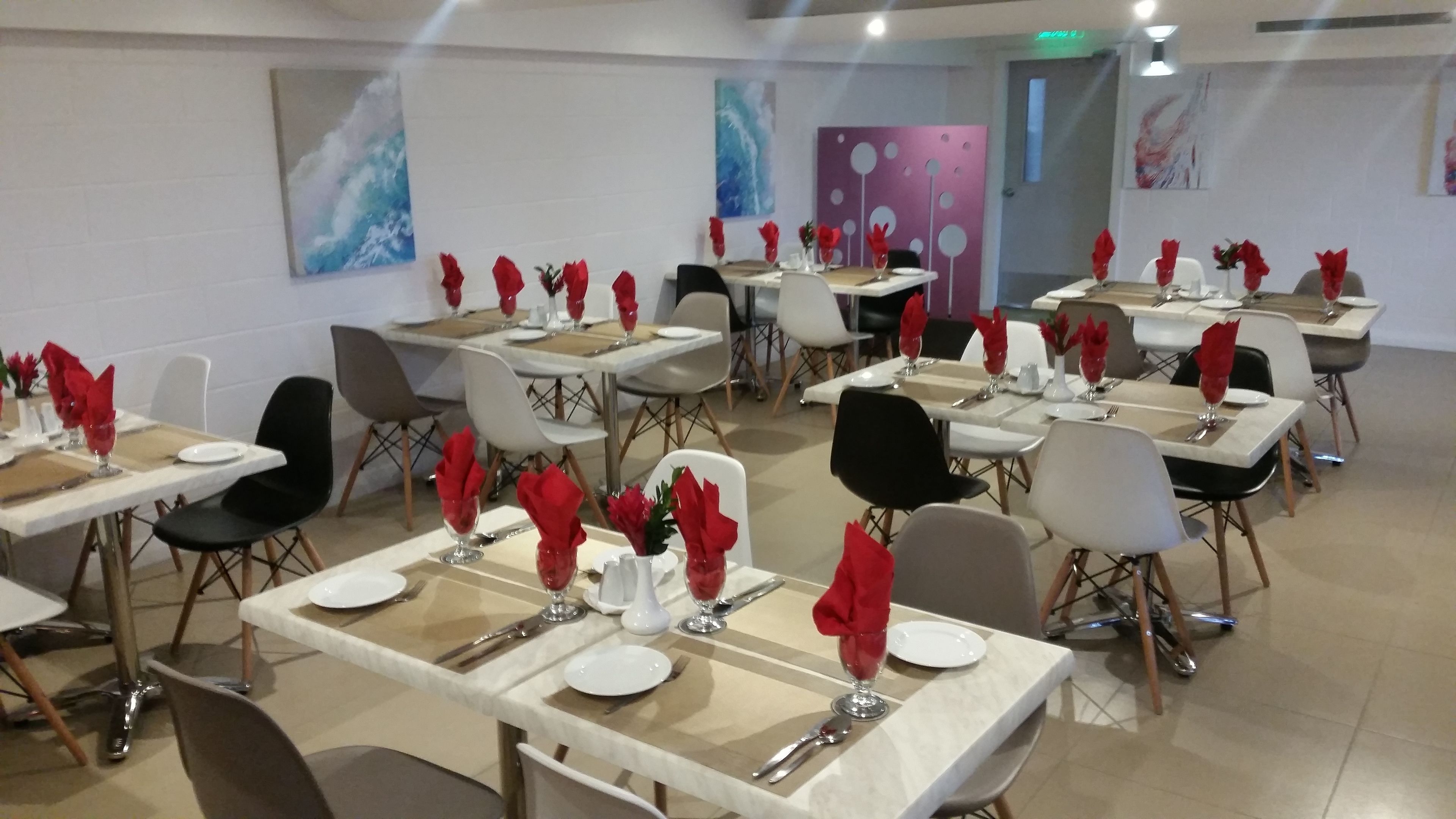 A dining area with multiple tables set for service, each with white plates, cutlery, and red napkins.