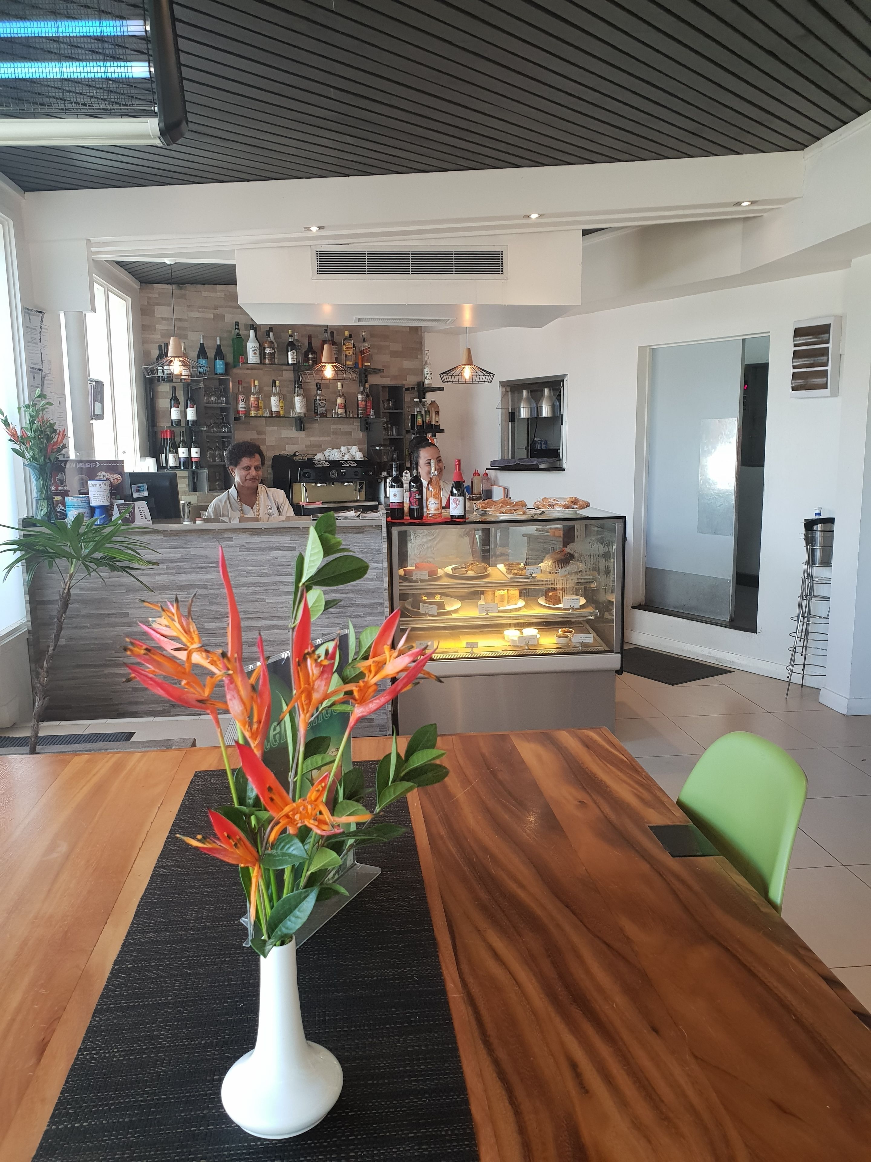 A modern interior with a wooden table, a vase with flowers, and a counter displaying pastries.