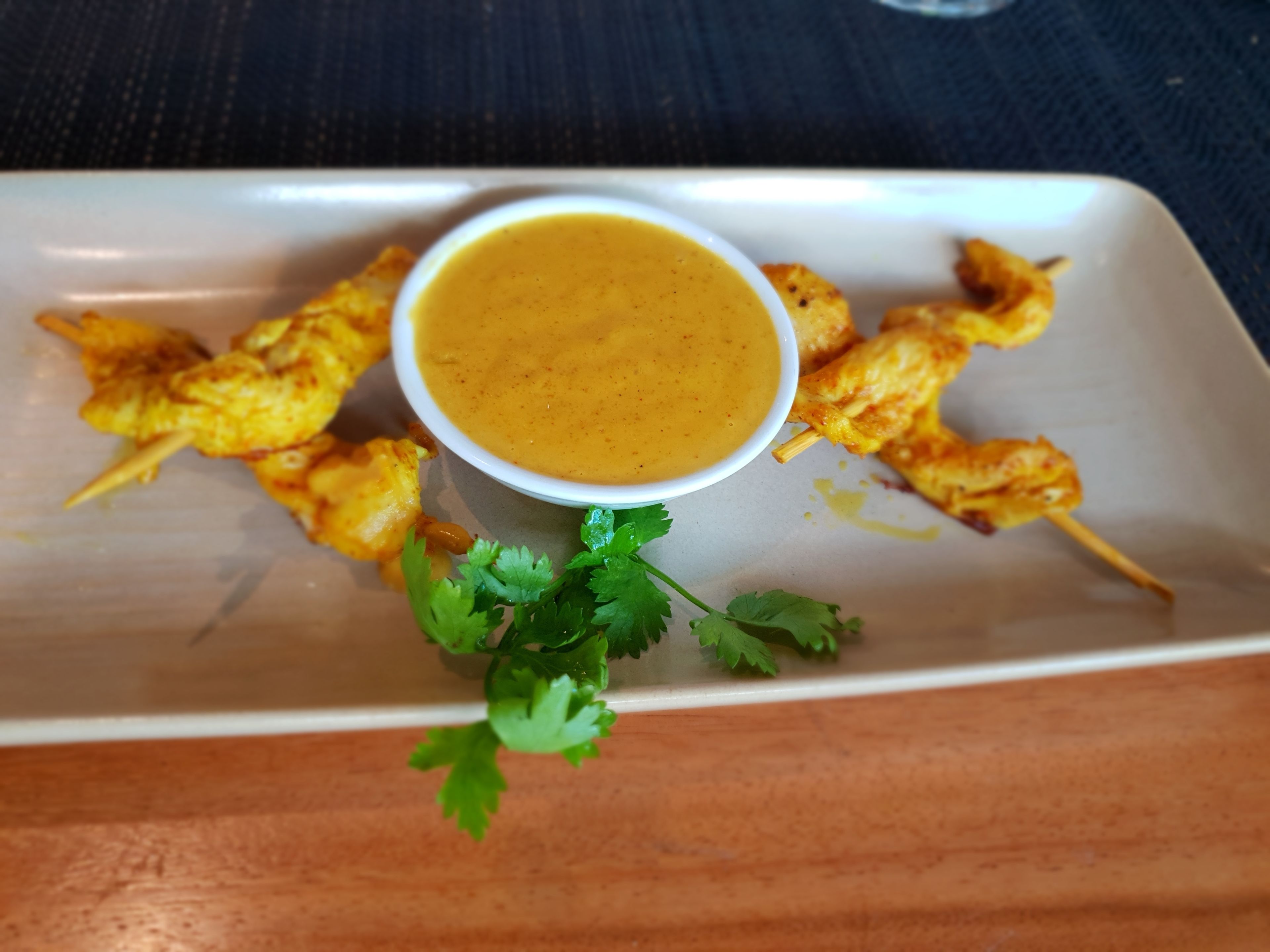 A plate with grilled chicken skewers and a bowl of sauce, garnished with cilantro.