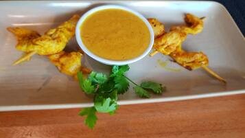 A plate with grilled chicken skewers and a bowl of sauce, garnished with cilantro.