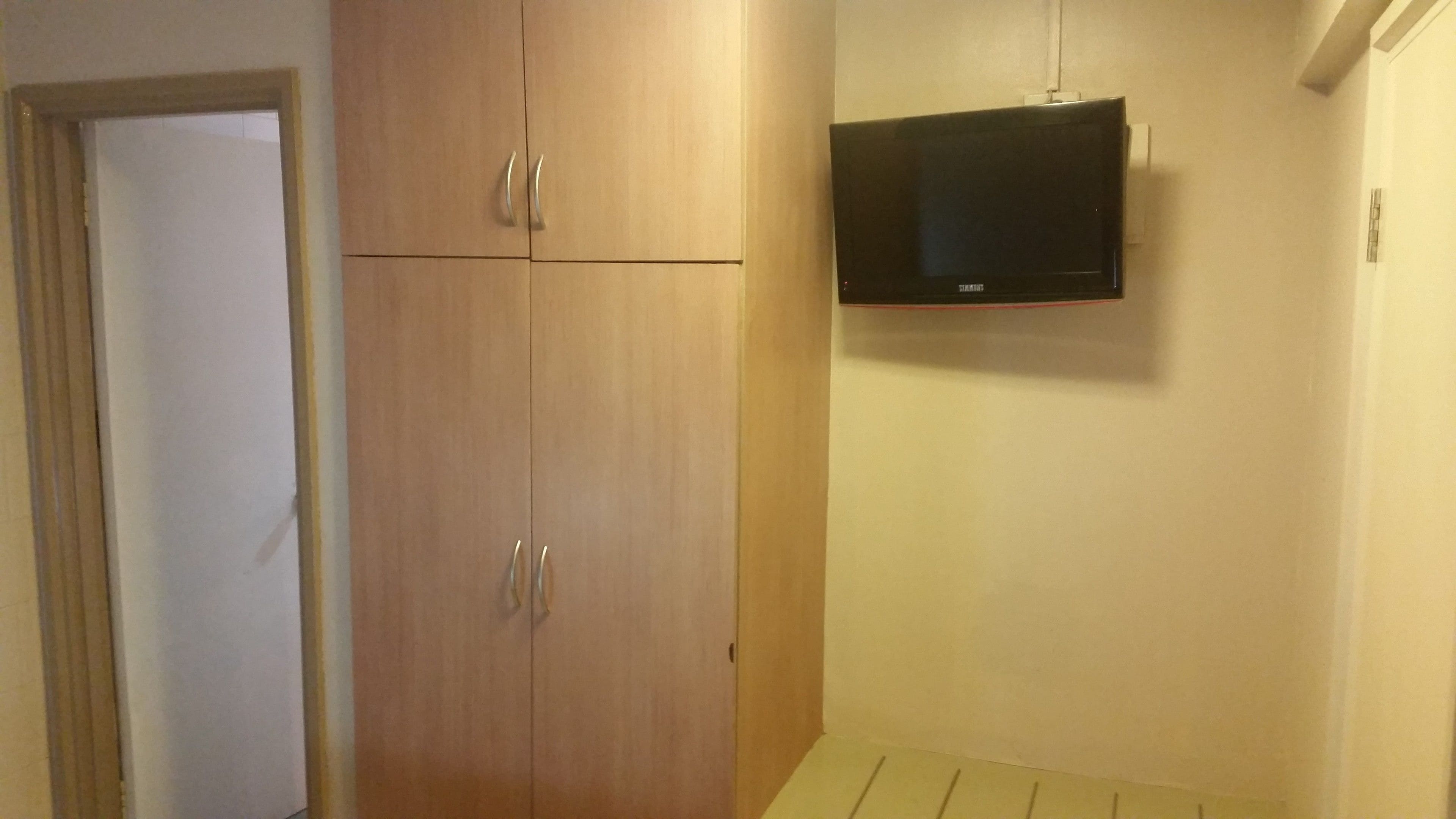 A room with a wooden wardrobe, a television mounted on the wall, and a door.