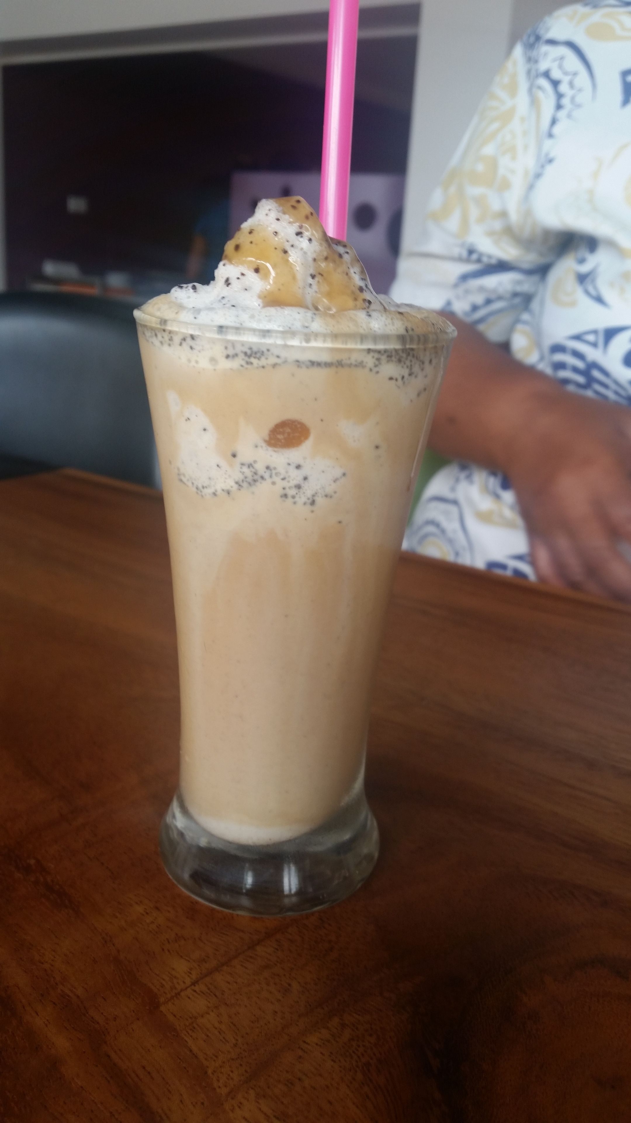 A glass of iced coffee with whipped cream and a pink straw on a wooden table.