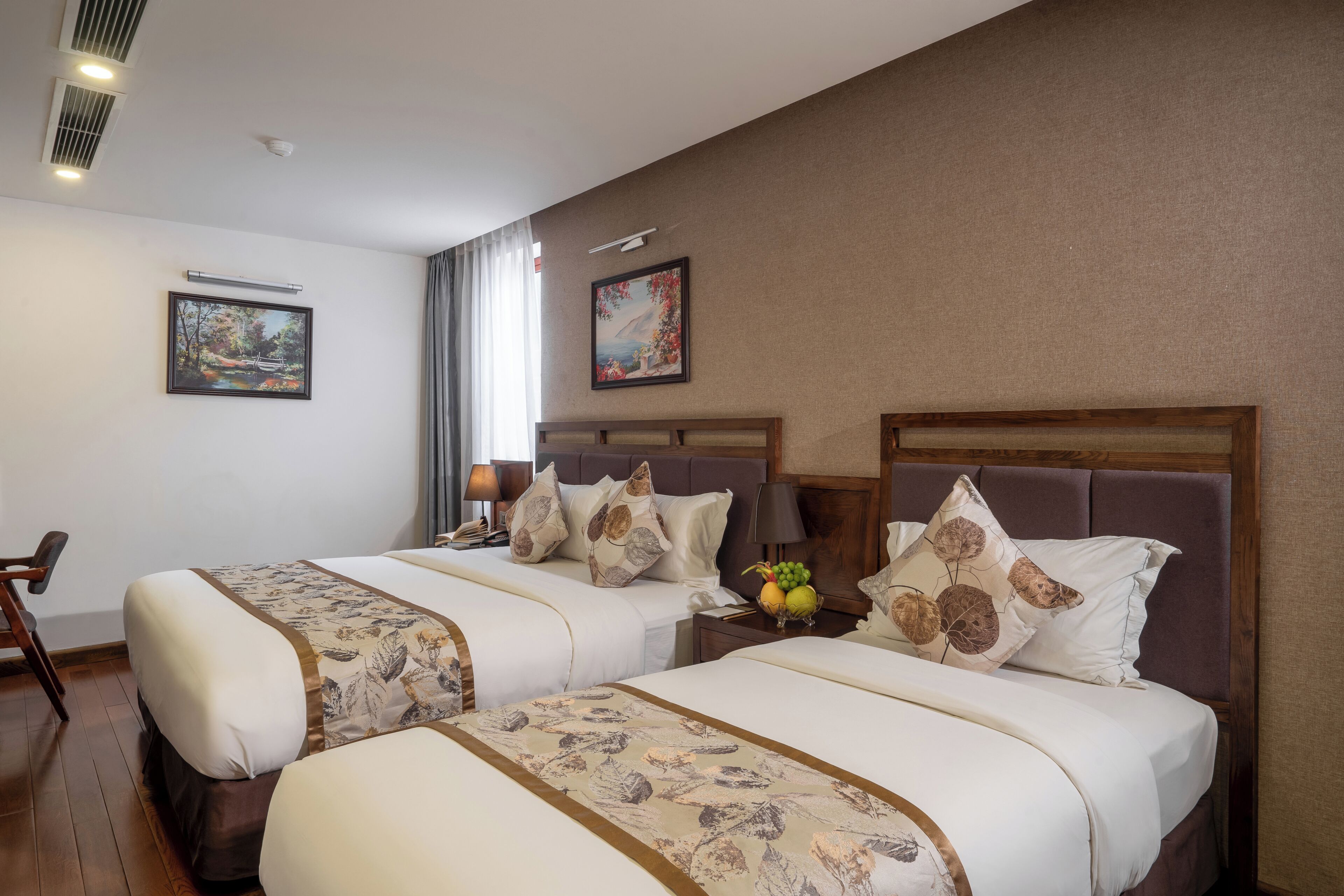 A hotel room with two beds, a nightstand, a lamp, and two framed pictures on the wall.