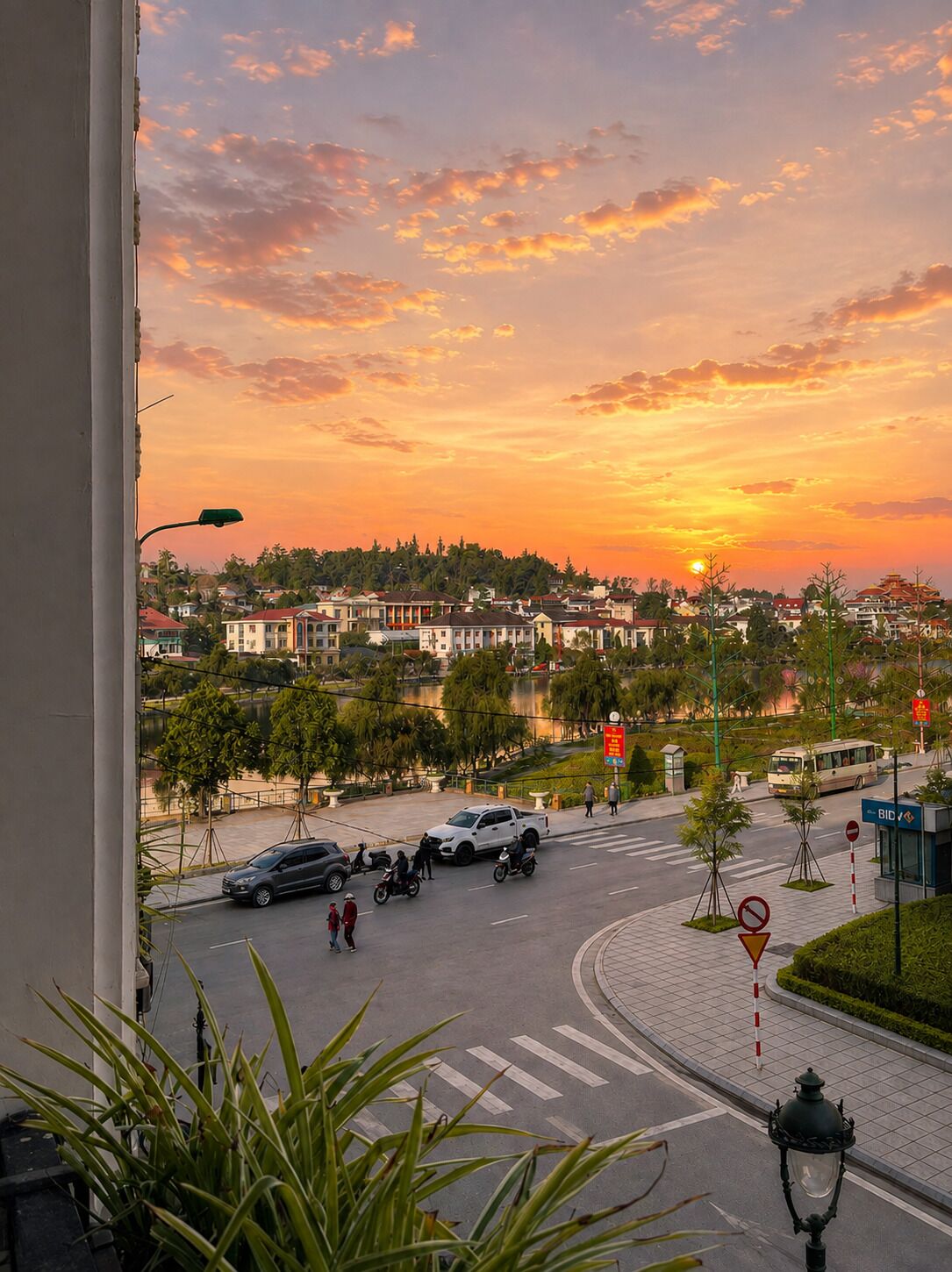 A view of a street with vehicles and pedestrians, a roundabout, and buildings in the background.