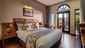 A hotel room with a large bed, wooden headboard, a nightstand with a lamp, a painting on the wall, and a balcony with a view. - Canvas Sapa Legend Hotel (Sa Pa)