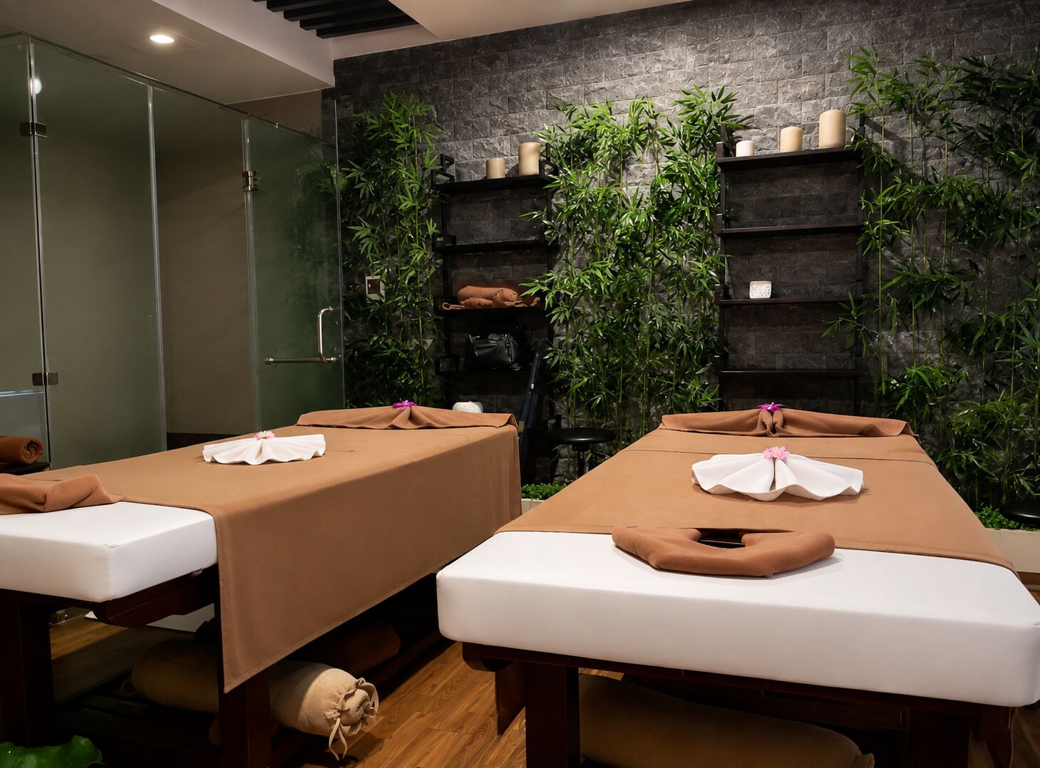 A spa room with two massage tables, a stone wall, and bamboo plants.
