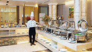 A buffet setup with multiple serving stations, a chef, and a decorative wall with a patterned design. - Canvas Sapa Legend Hotel (Sa Pa)