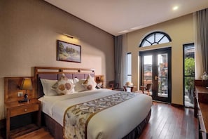 Habitación de hotel con una cama grande, una mesita de noche, un cuadro en la pared y vistas al exterior a través de una puerta.