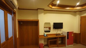 Una habitación pequeña con un armario de madera, un escritorio con espejo, televisión y un refrigerador rojo.