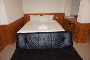 A hotel room with a bed, a wooden headboard, a black leather sofa, and a small wooden table with a pillow on it. - Loei Residence (Mueang Loei)