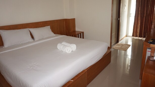 Habitación de hotel con una cama grande, cabecera de madera, ropa de cama blanca y una mesita de noche de madera.