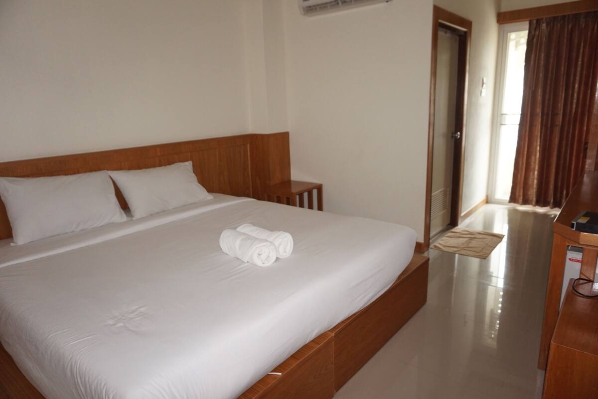Une chambre d’hôtel avec un grand lit, une tête de lit en bois, du linge de lit blanc et une table de chevet en bois.