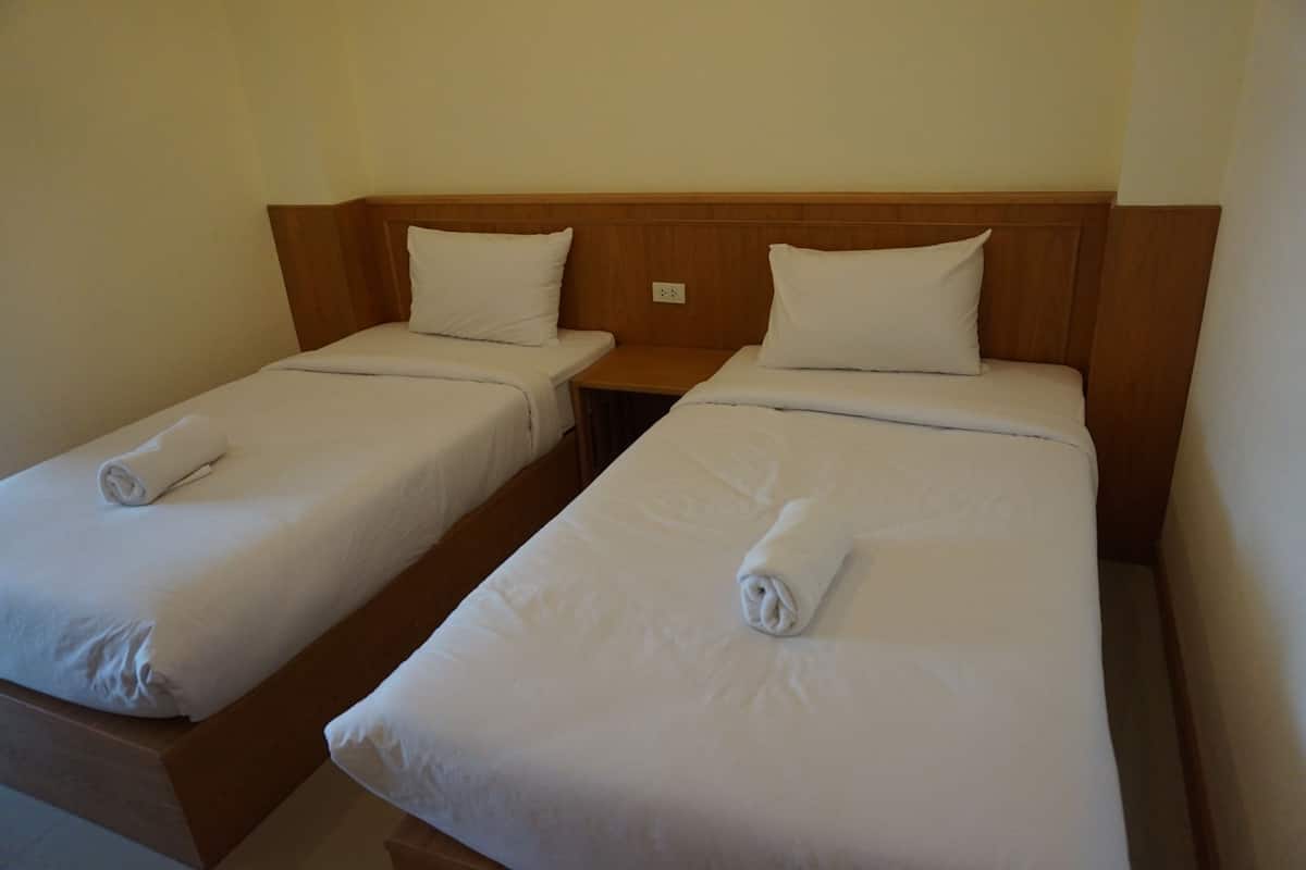 Deux lits simples avec des têtes de lit en bois, du linge de lit blanc et des serviettes enroulées.