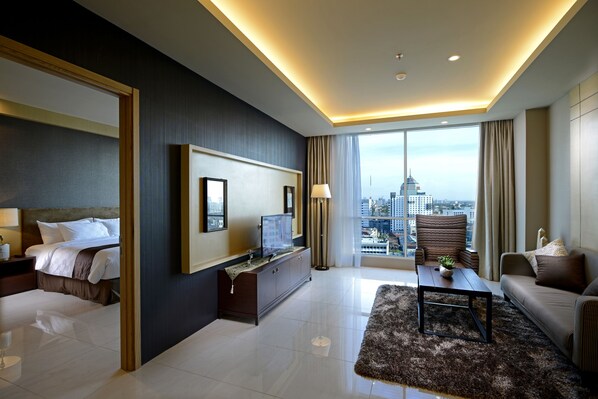 A modern hotel room with a bed, a TV, a sofa, a coffee table, and a large window offering a city view.
