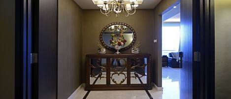 A hallway with a marble floor, a dark wooden console table with a mirror, and a chandelier.