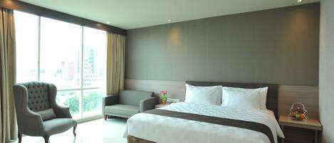 Habitación de hotel con una cama grande, un sofá, una silla y una mesita de noche con fruteros.