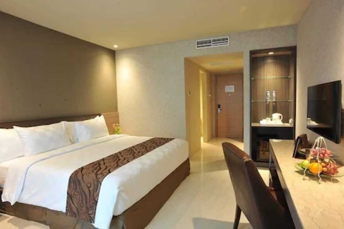 Ein Hotelzimmer mit einem großen Bett, einem Schreibtisch mit Stuhl, einem Fernseher und einer kleinen Küchenzeile.