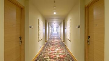 Un largo pasillo con alfombra estampada, puertas de madera y una serie de lámparas a lo largo del techo.