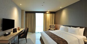 Ein Hotelzimmer mit Bett, Schreibtisch mit Stuhl, Fernseher und einem großen Fenster mit Vorhängen.