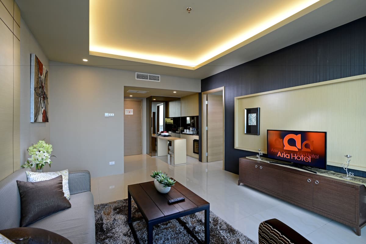 Ein modernes Hotelzimmer mit Wohnbereich, ausgestattet mit einer Couch, einem Couchtisch und einem Fernseher auf einem Holzkasten.