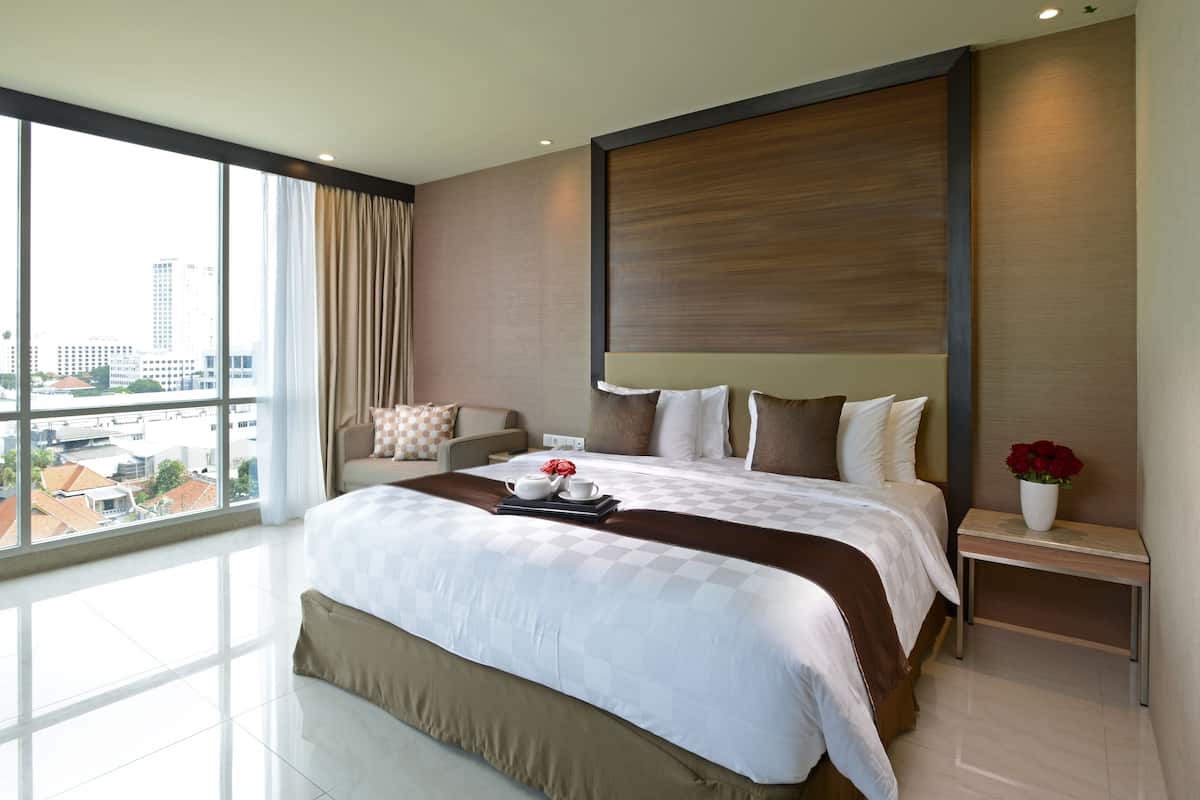 Ein modernes Hotelzimmer mit einem großen Bett, einem Nachttisch, einem Fenster mit Blick auf die Stadt und einem kleinen Tisch mit Blumen.