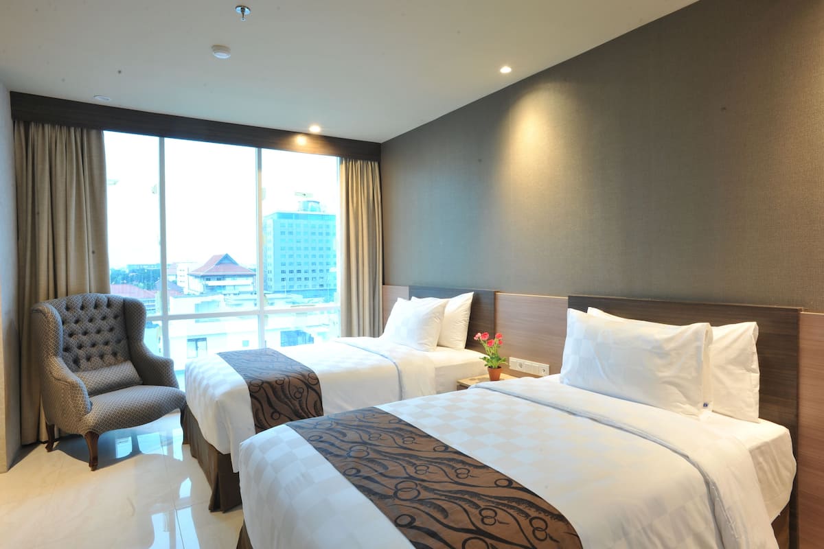 Ein Hotelzimmer mit zwei Betten, einem großen Fenster und Blick auf die Stadt.