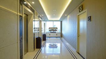 A modern hotel corridor with a reflective floor, a large window at the end, and a door marked with the number 18.