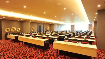 Un salón de conferencias con varias mesas y sillas dispuestas en filas, con una alfombra estampada e iluminación en el techo.