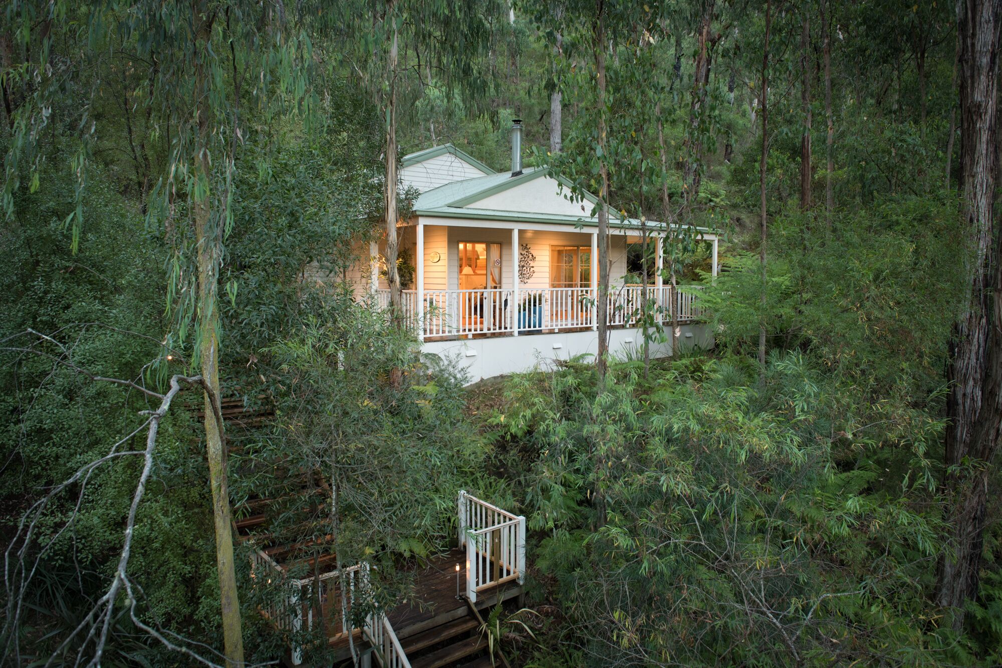 A cabin surrounded by dense forest, with a porch and a small deck.
