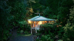A house surrounded by dense forest, with a visible porch and steps leading to the entrance. - Myers Creek Cascades Luxury Cottages (Healesville)