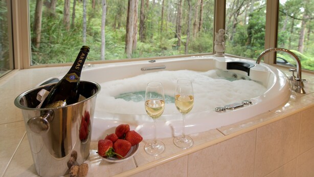 A hot tub with champagne and strawberries, a bottle of champagne, and a bowl of strawberries. - Myers Creek Cascades Luxury Cottages (Healesville)