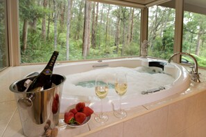 A hot tub with champagne and strawberries, a bottle of champagne, and a bowl of strawberries. - Myers Creek Cascades Luxury Cottages (Healesville)