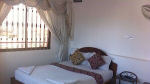 A single bed with a wooden frame, a white bedspread, and two decorative pillows. There is a small wooden nightstand beside the bed. - Royal Guest House (Phnom Penh)