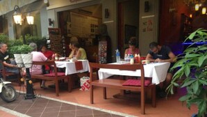 An outdoor dining area with tables and chairs, a potted plant, and a motorcycle parked outside. - Royal Guest House (Phnom Penh)