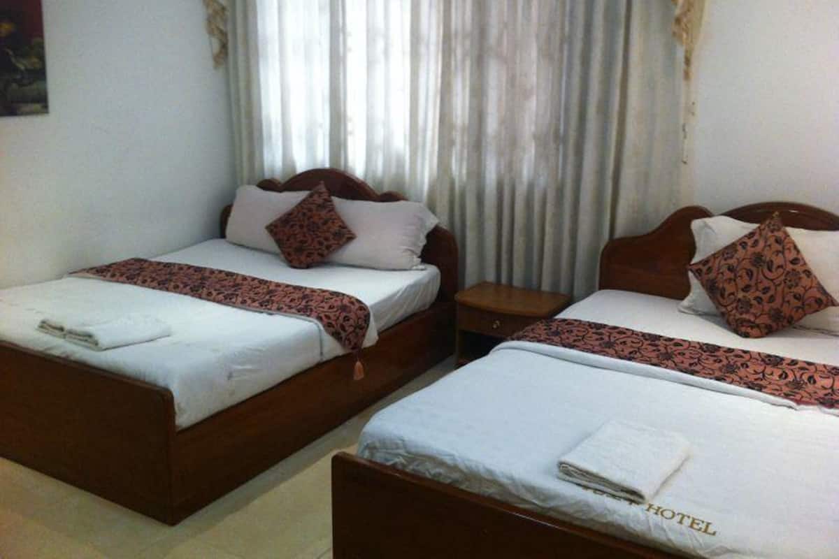 A hotel room with two single beds, each with a wooden headboard, white linens, and patterned throw blankets.