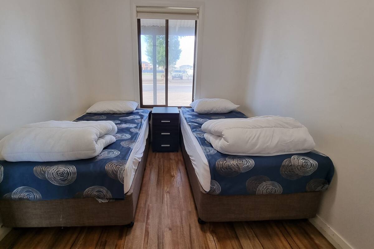 A narrow room with two beds, a small table, and a window.