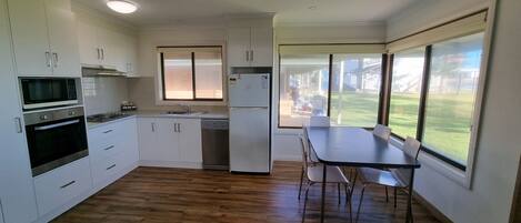 A compact kitchen with white cabinets, a microwave, an oven, a refrigerator, and a dining table with chairs.