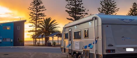 Una caravana estacionada en un camping con un atardecer de fondo.