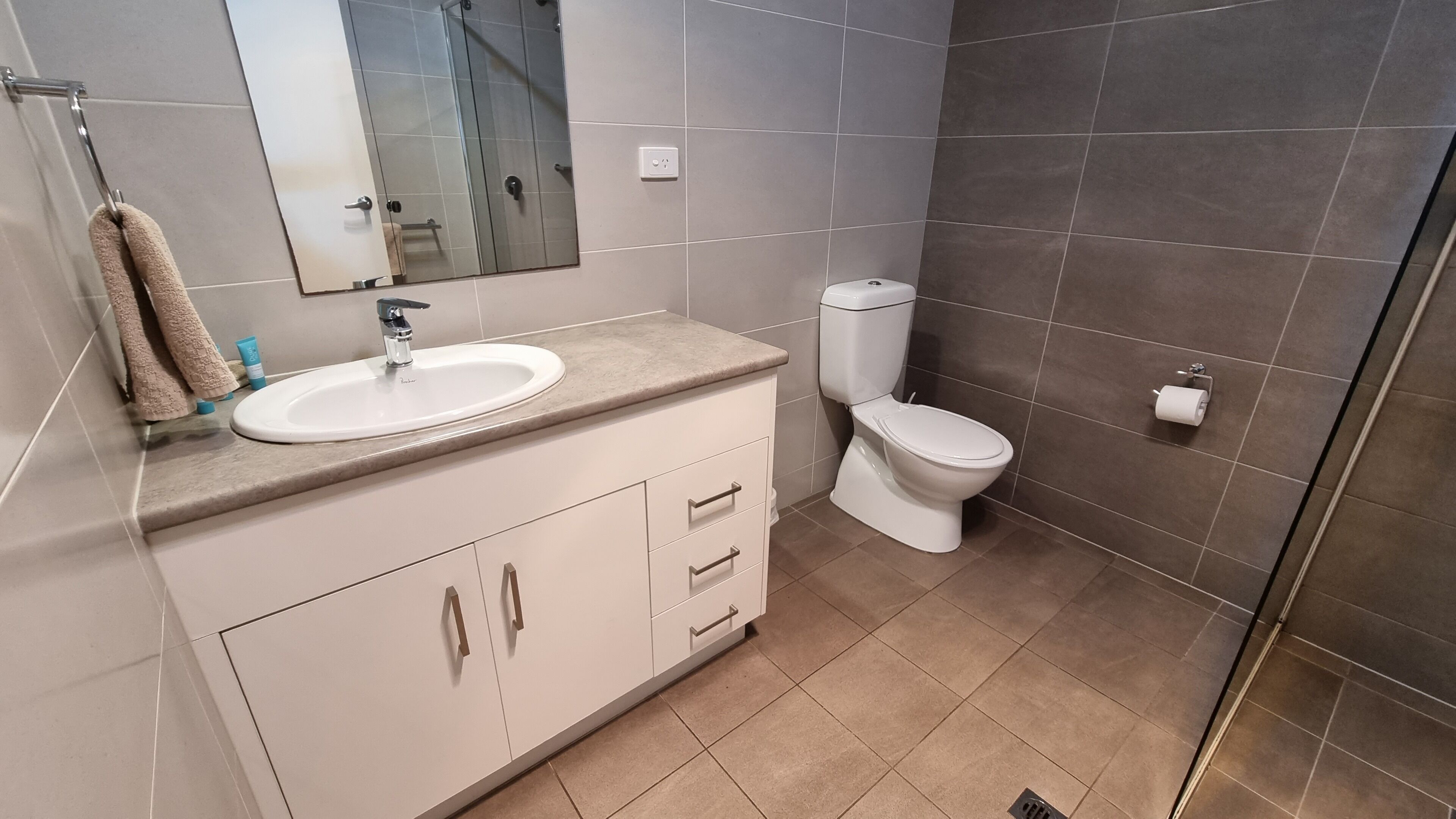 A modern bathroom with a sink, mirror, toilet, and shower area.