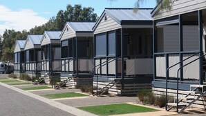 A row of modern, single-story mobile homes with external staircases, set against a backdrop of trees and a clear sky. - Wallaroo Holiday Park (Wallaroo)