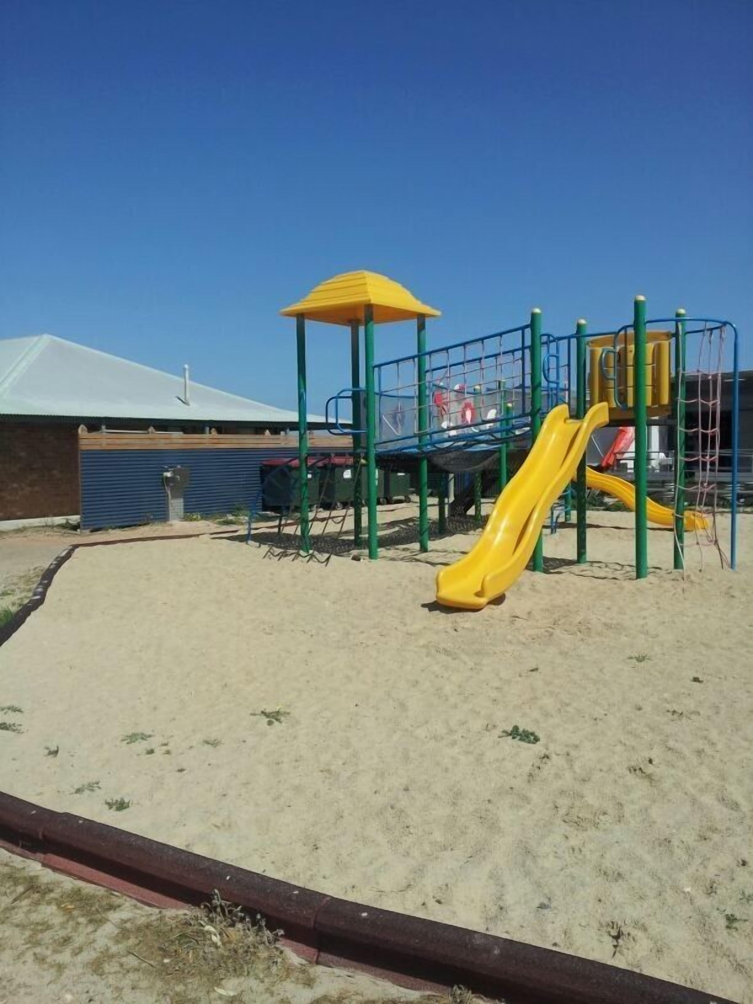 A playground with a yellow slide and a climbing structure.