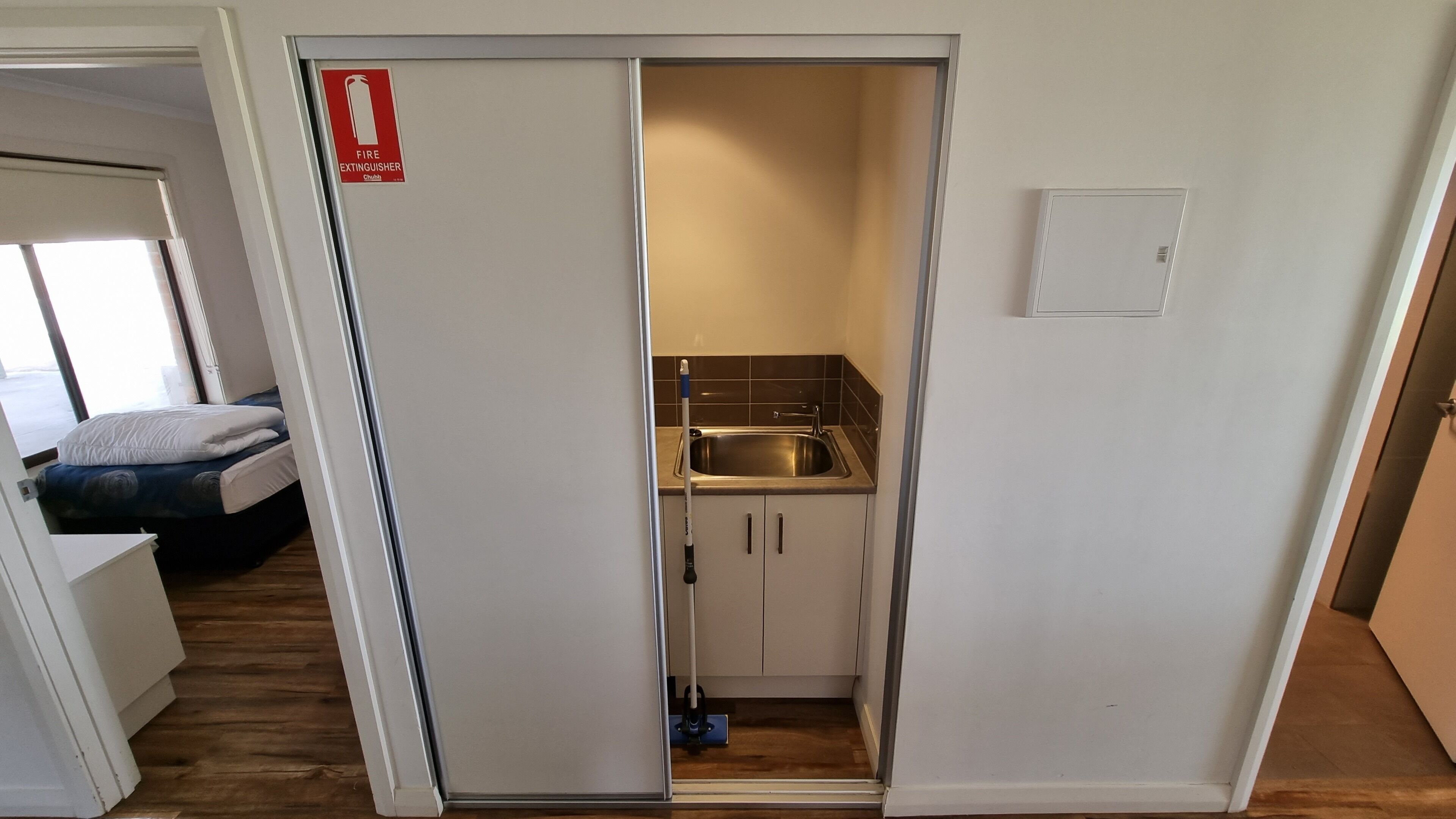 Habitación compacta con kitchenette, una cama y señalización de extintor visible.
