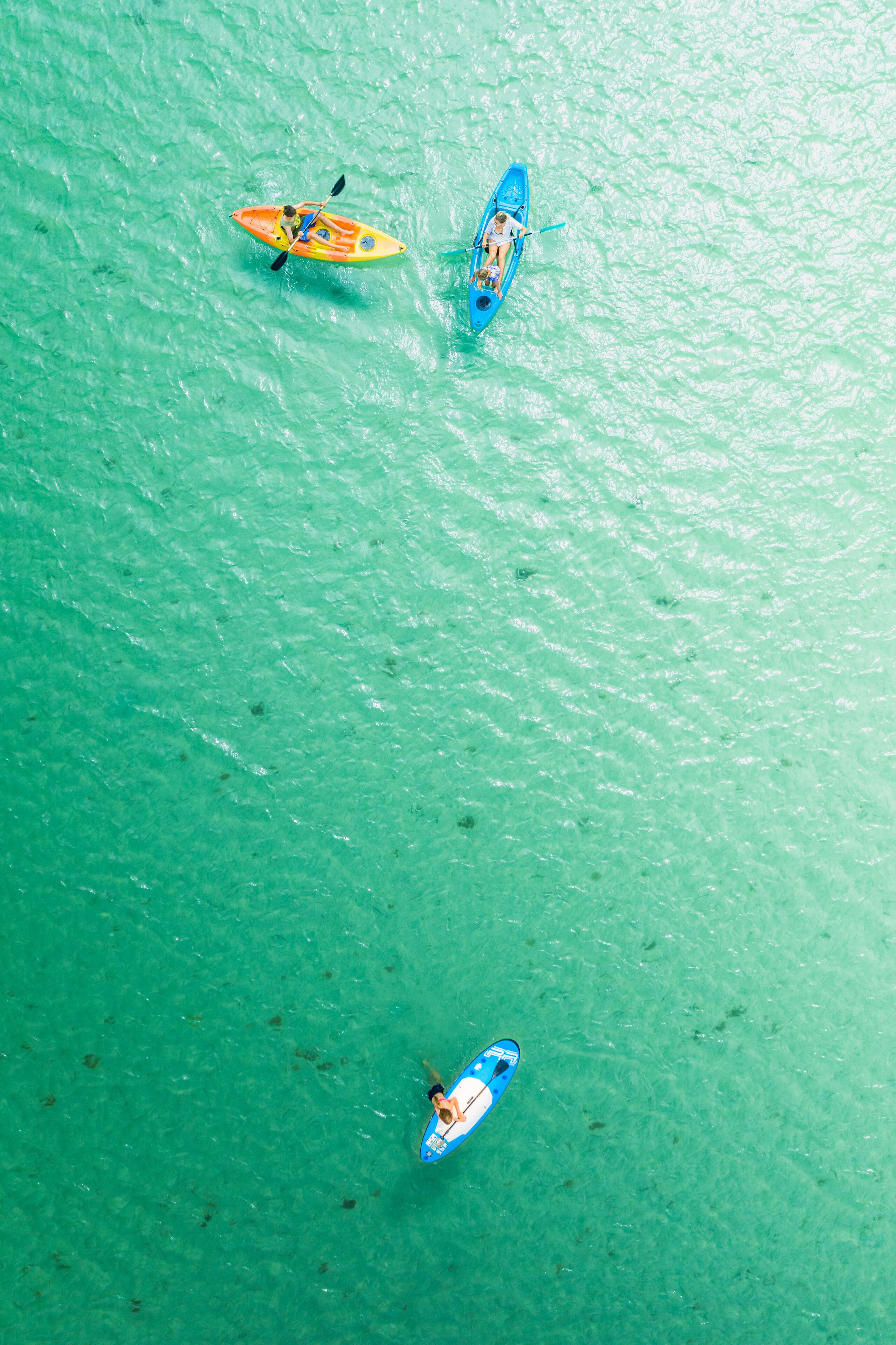 An aerial view of a turquoise body of water with three kayaks.