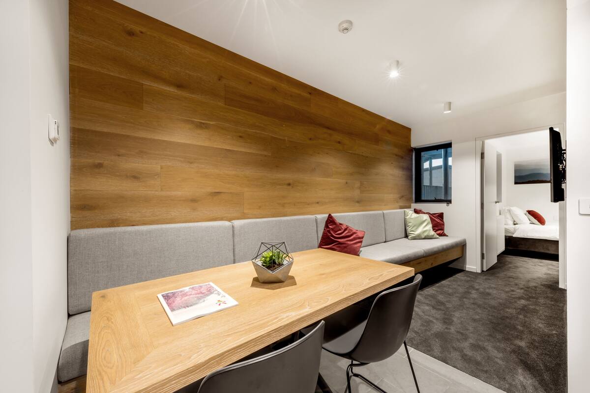 A modern living room with a wooden accent wall, grey sofa, and a dining table with chairs.