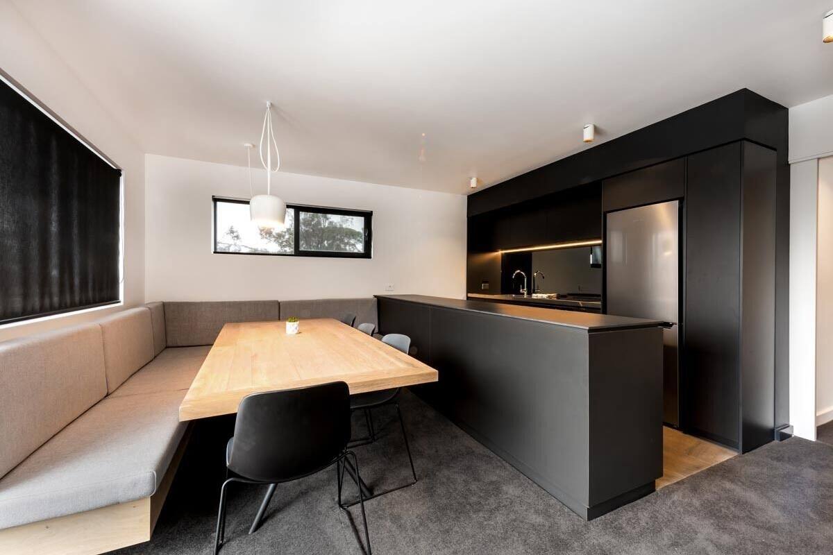 A modern kitchen with a built-in island, a dining area with a wooden table and black chairs, and a large window with curtains.