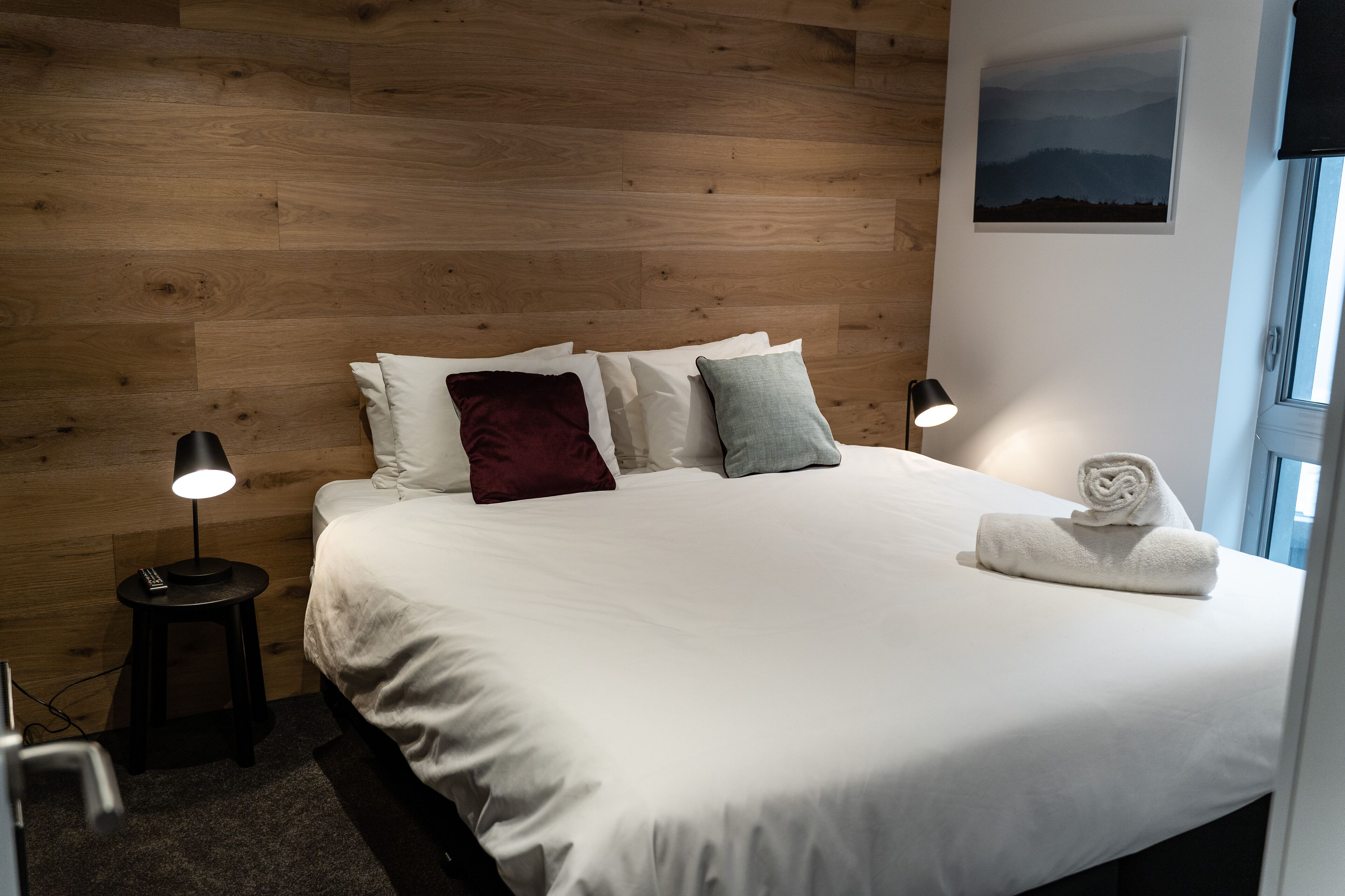 A neatly made bed with white bedding, a red pillow, and two side tables with lamps.
