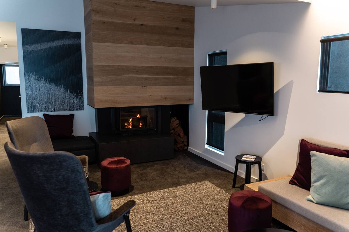 A modern living room with a fireplace, a flat-screen TV mounted on the wall, and a sofa with cushions.