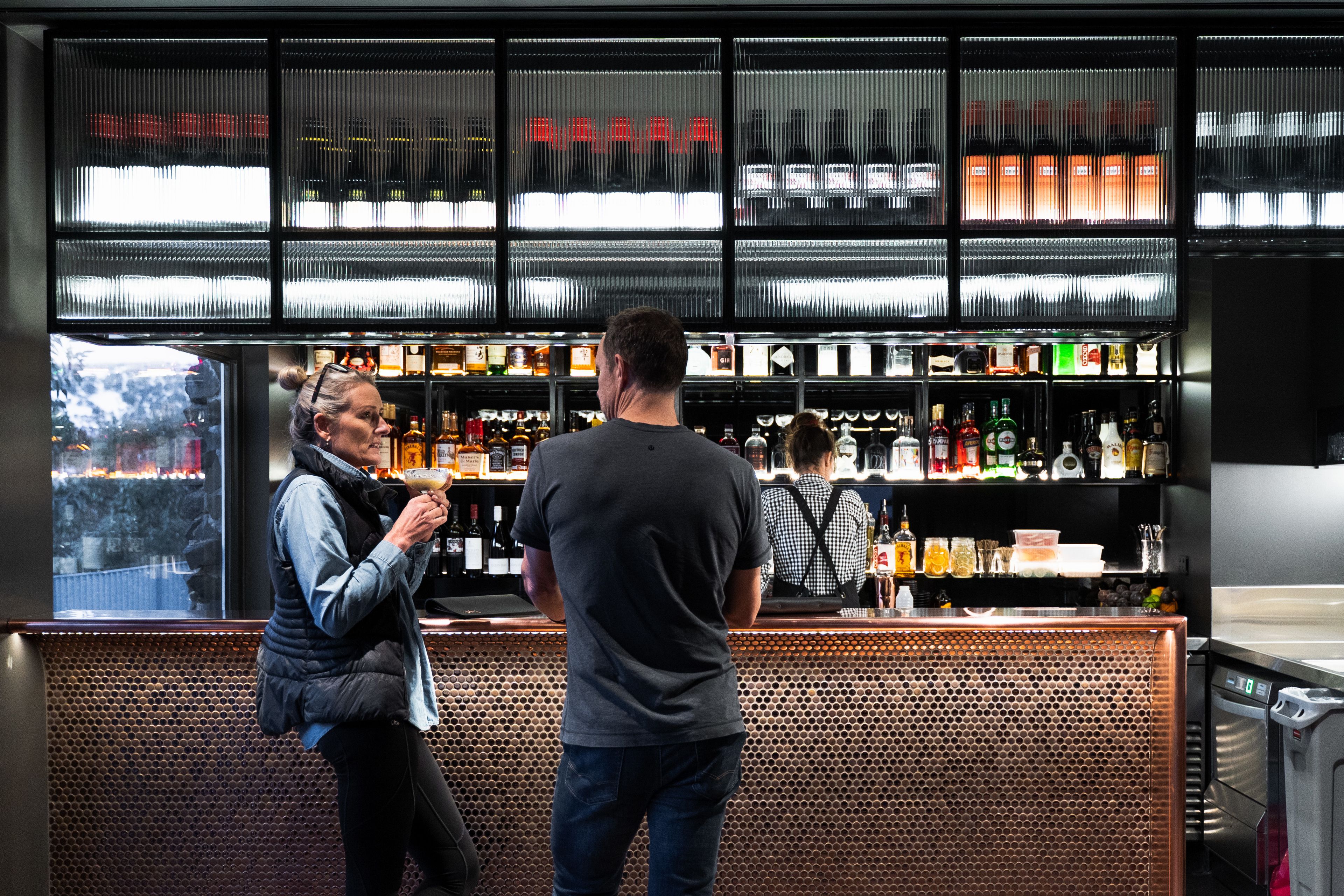 A bar area with a metal mesh partition, shelves with bottles, and a window view.