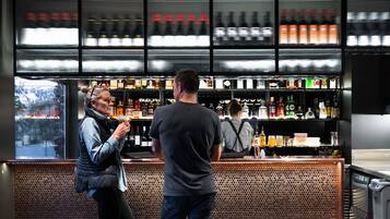 A bar area with a metal mesh partition, shelves with bottles, and a window view.