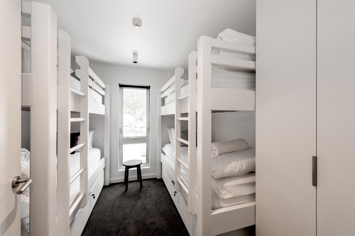 A narrow room with bunk beds, a small stool, and a window.
